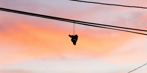 A pair of trainers or sneakers hangs over a telephone wire by the laces against a dawn or dusk sky