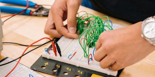 A person's hands adjust wires on a rudimentary computer