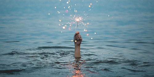 Person submerged in water holding up a sparkler