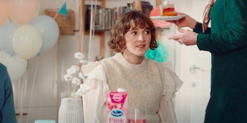 A woman sits at a table at a party with a carton of juice in front of her