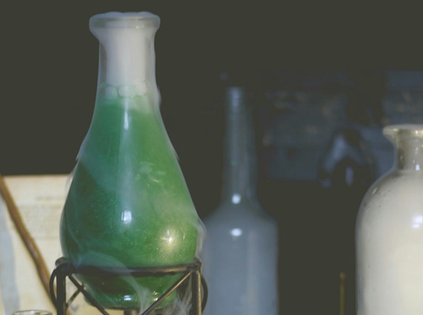 A glass flask containing a green liquid surrounded by a white vapour