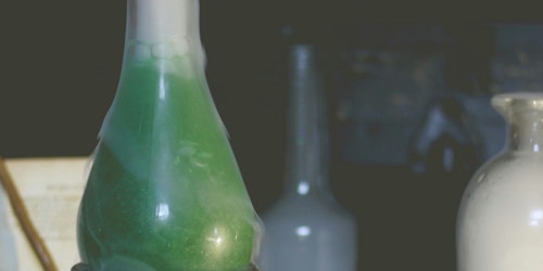 A glass flask containing a green liquid surrounded by a white vapour