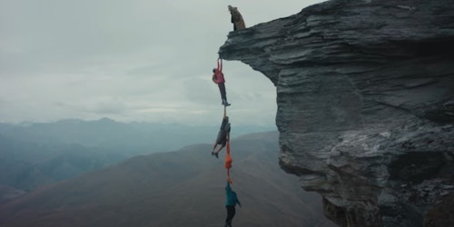 Three hikers dangling over the edge of a cliff using Macpac garments as ropes