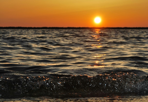 The sun low over the sea with waves breaking on the beach