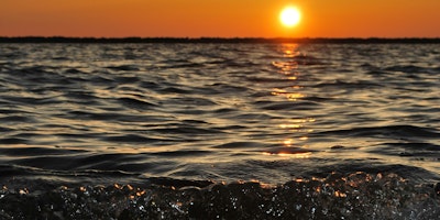 The sun low over the sea with waves breaking on the beach