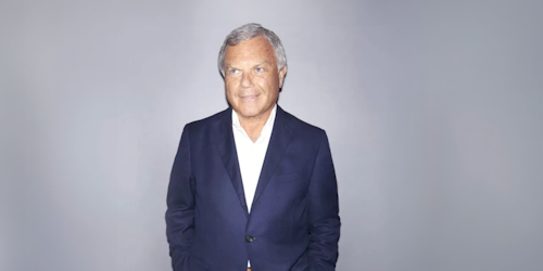 Sir Martin Sorrell, wearing a navy blue blazer with gray trousers and a white shirt open at the neck 